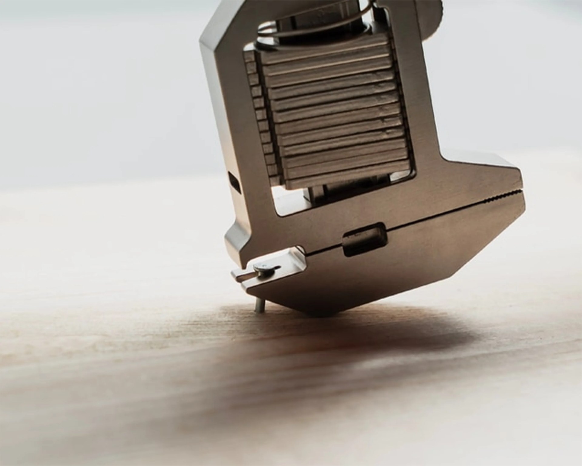 Close-up of a metal mechanical component with stacked plates and a small pin on a wooden surface.