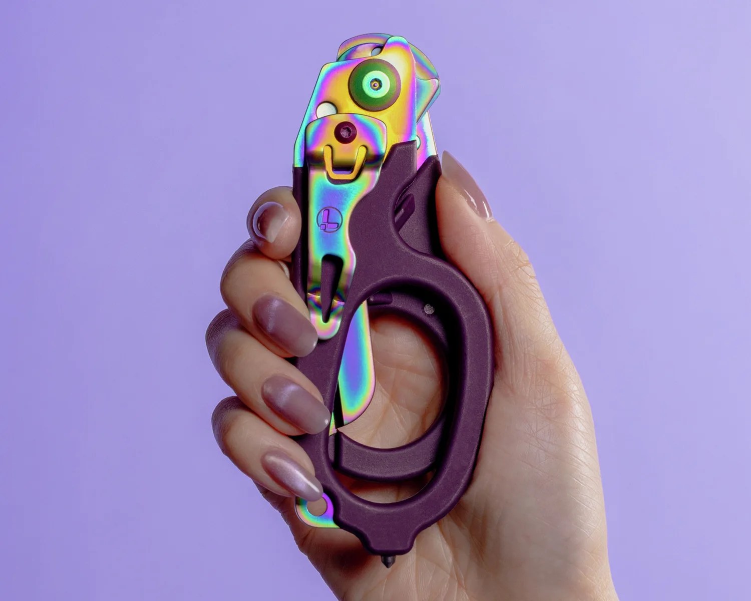 Hand holding a compact multi-tool with a purple handle and iridescent metal parts against a purple background.