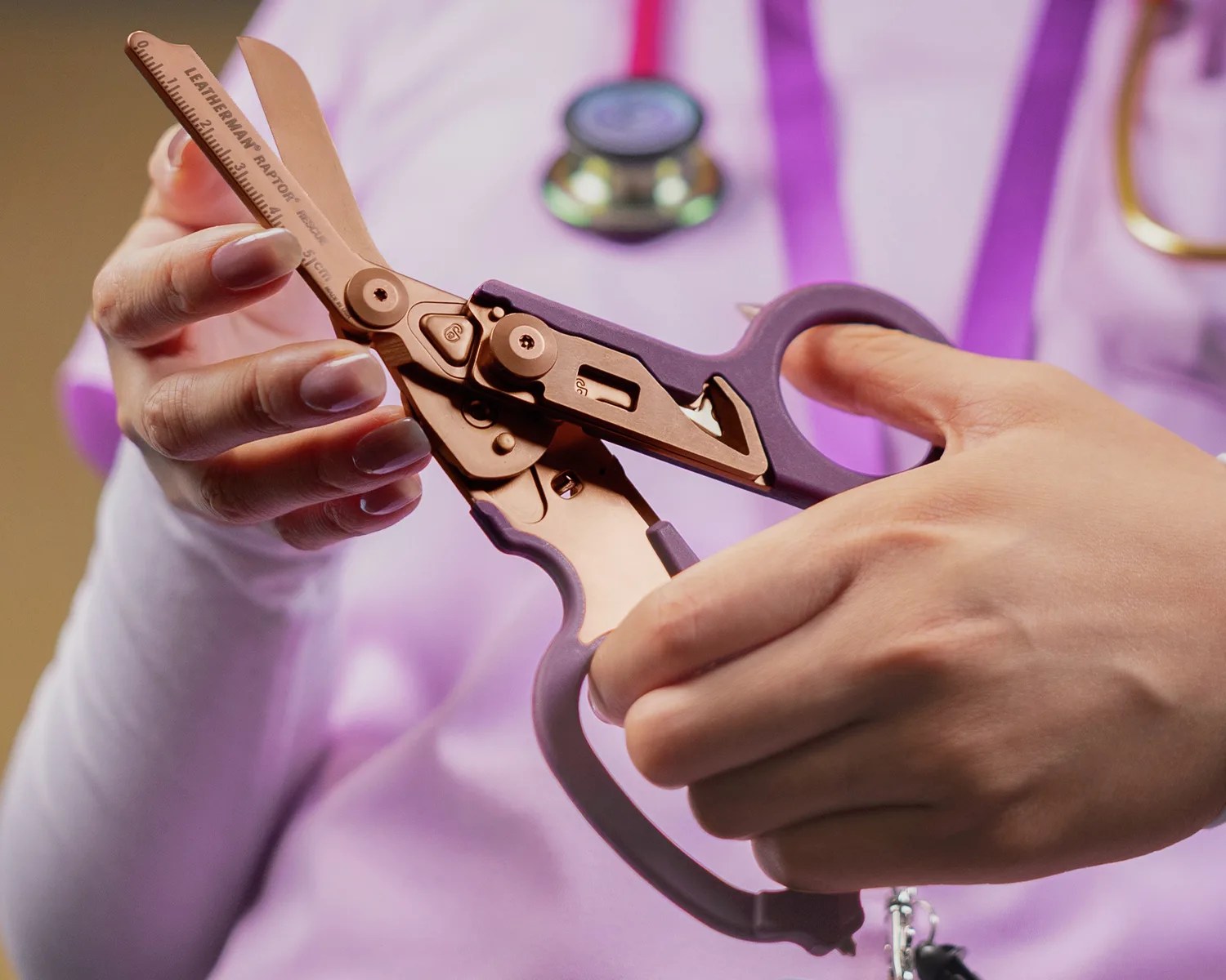 Hands holding a Leatherman Raptor multi-tool with purple handles and a ruler on the blade.