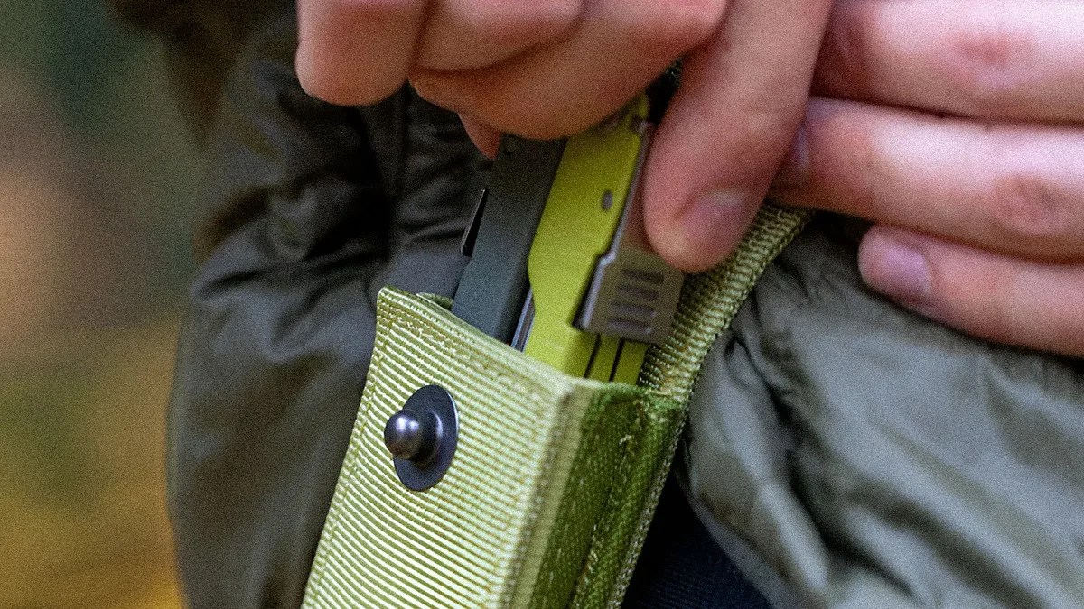 Hand placing a green multi-tool into a green fabric sheath with a snap button.