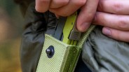 Hand placing a green multi-tool into a green fabric sheath with a snap button.