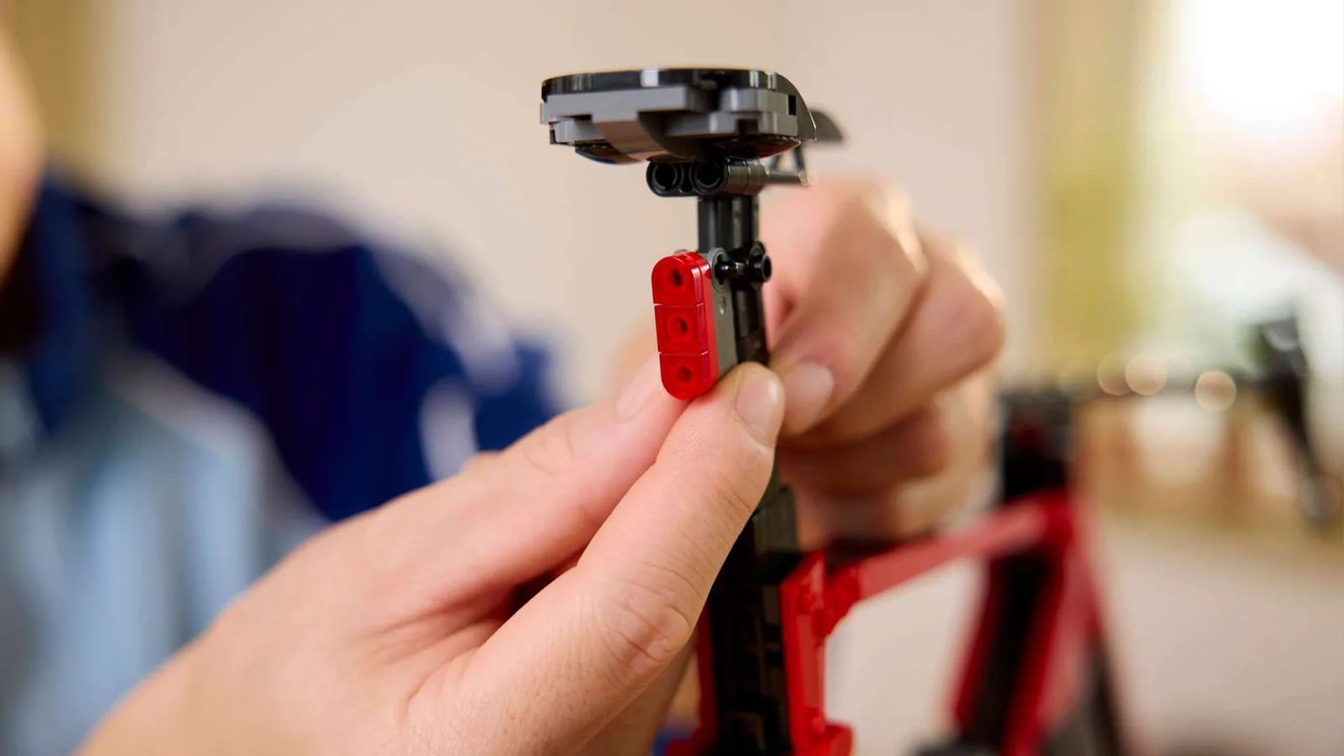 Hands assembling a black and red LEGO bicycle seat.