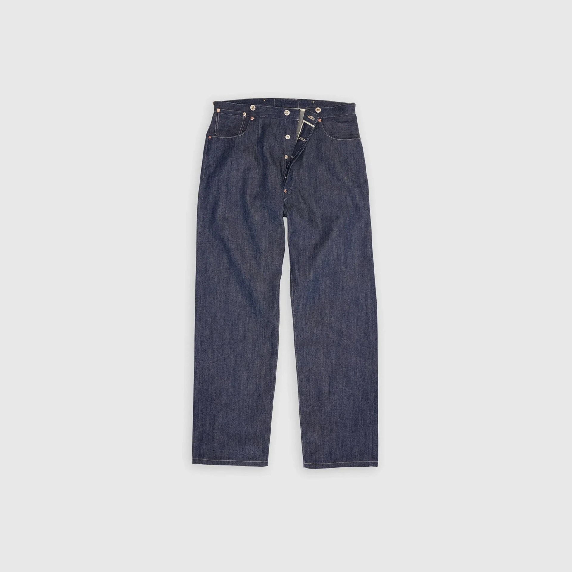 Dark blue denim jeans with button fly and copper rivets laid flat on a light background.