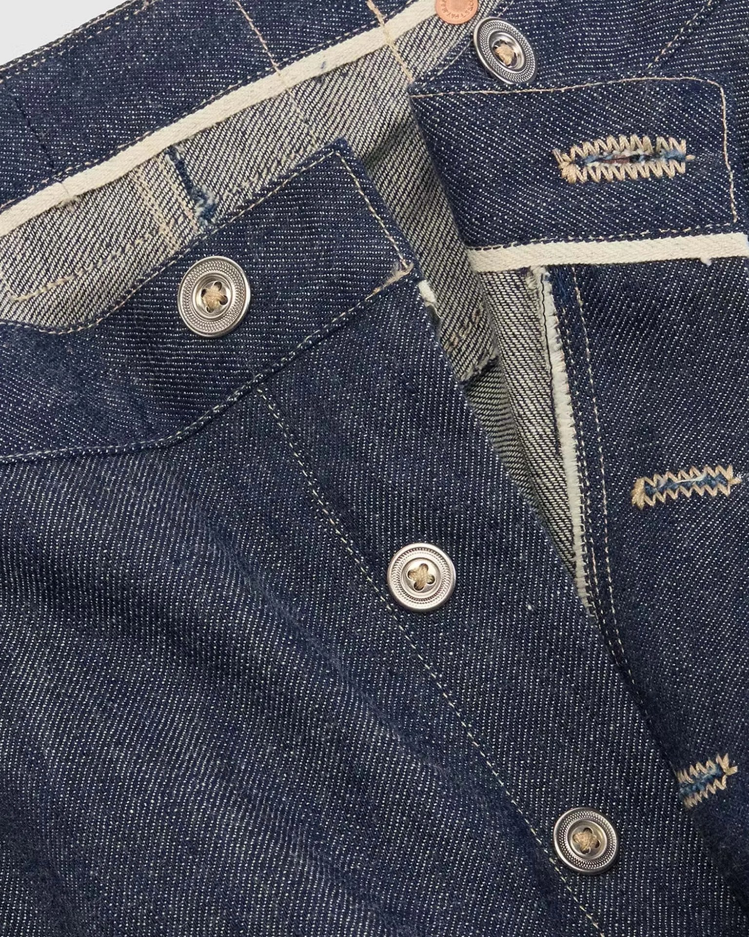 Close-up of dark blue denim fabric with silver buttons and beige stitching on a garment.
