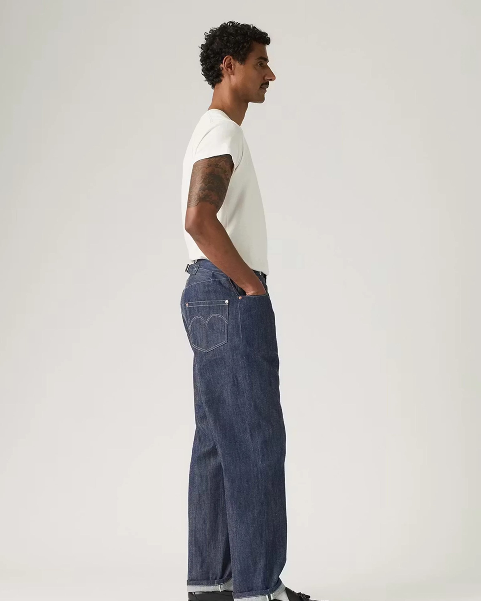 Man wearing white short-sleeve t-shirt and dark blue straight-leg jeans with rolled cuffs.