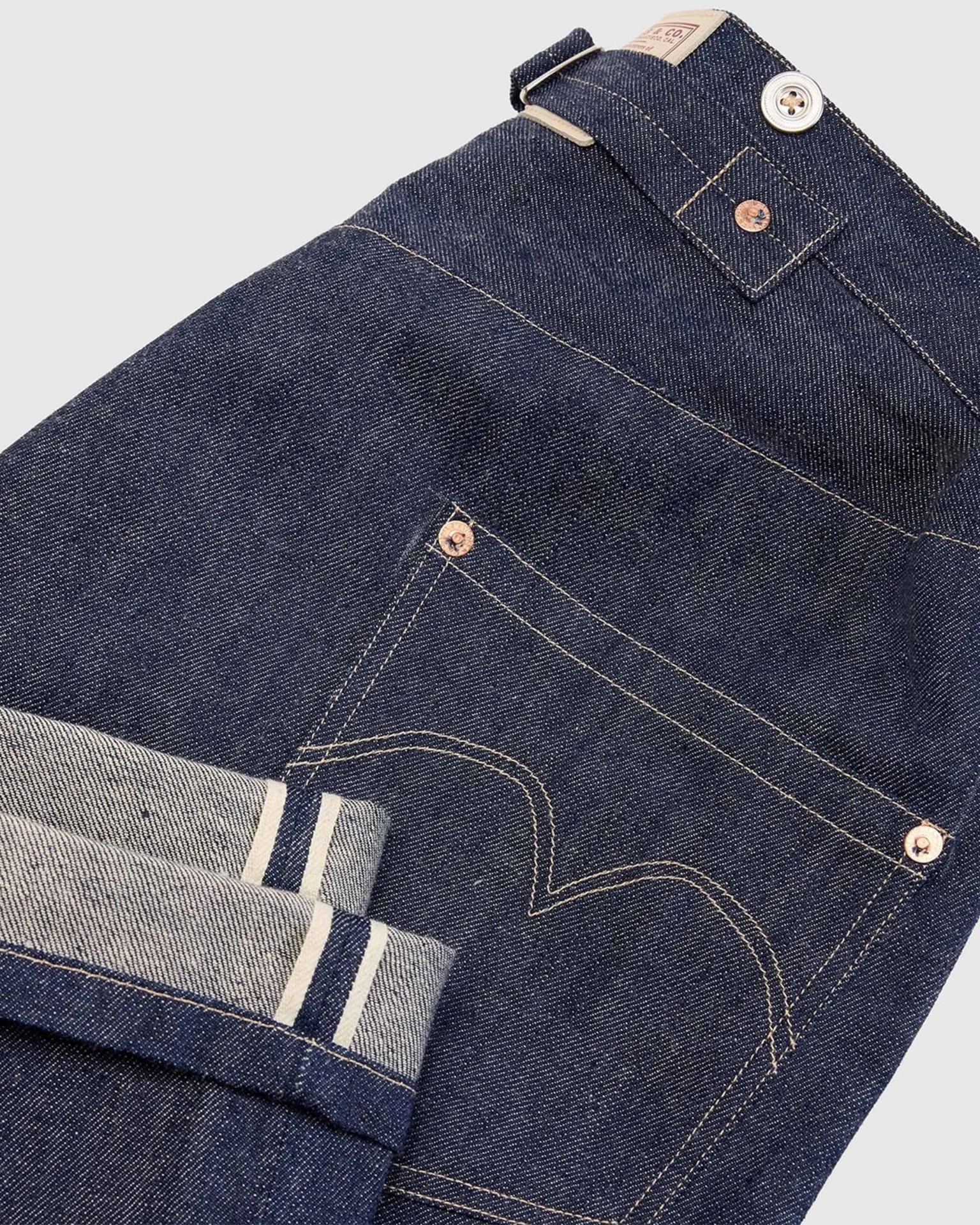 Dark blue selvedge denim jeans with visible white and blue selvedge edges and copper rivets.