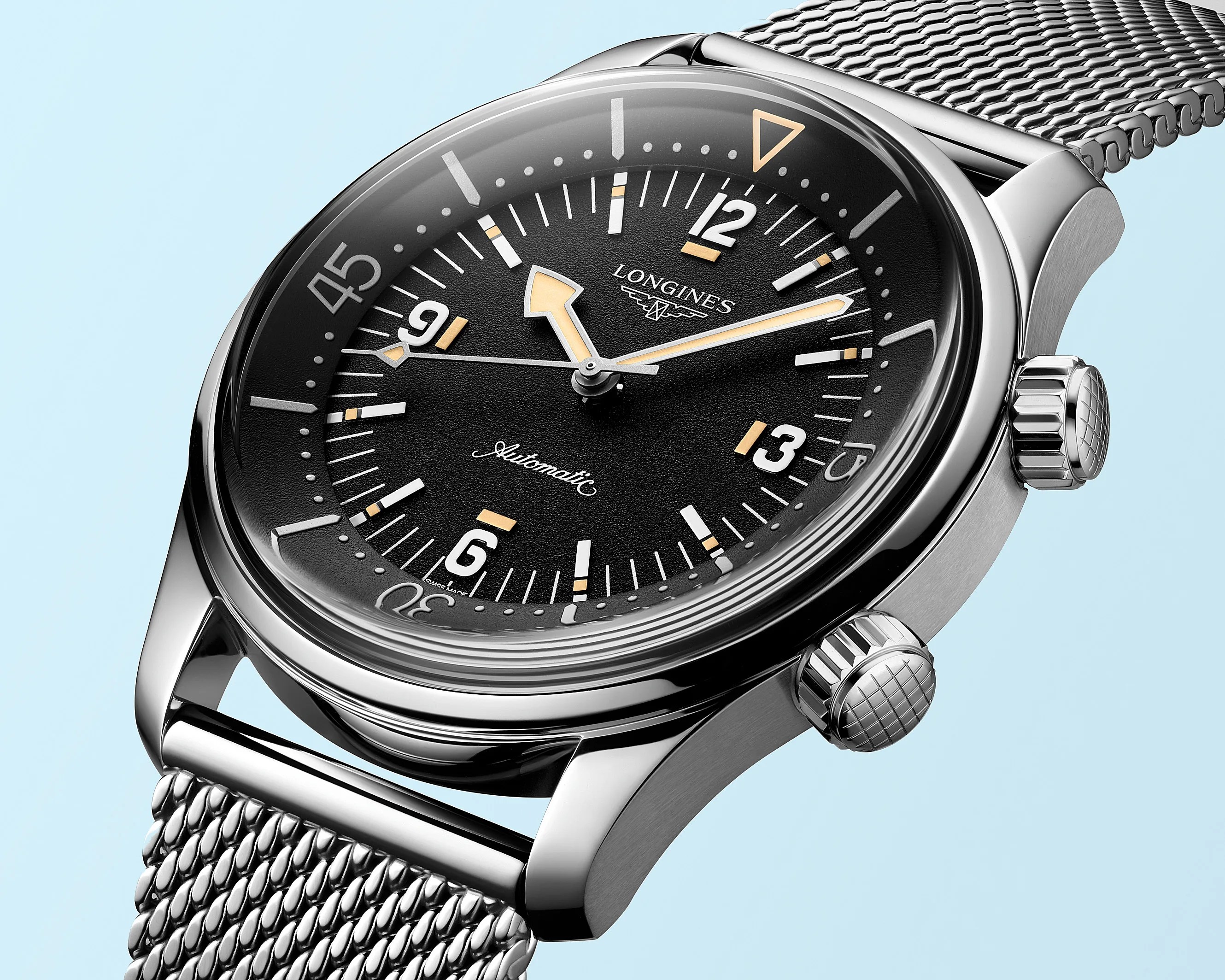 Close-up of a Longines automatic watch with a black dial, luminous hands, and a silver mesh bracelet.
