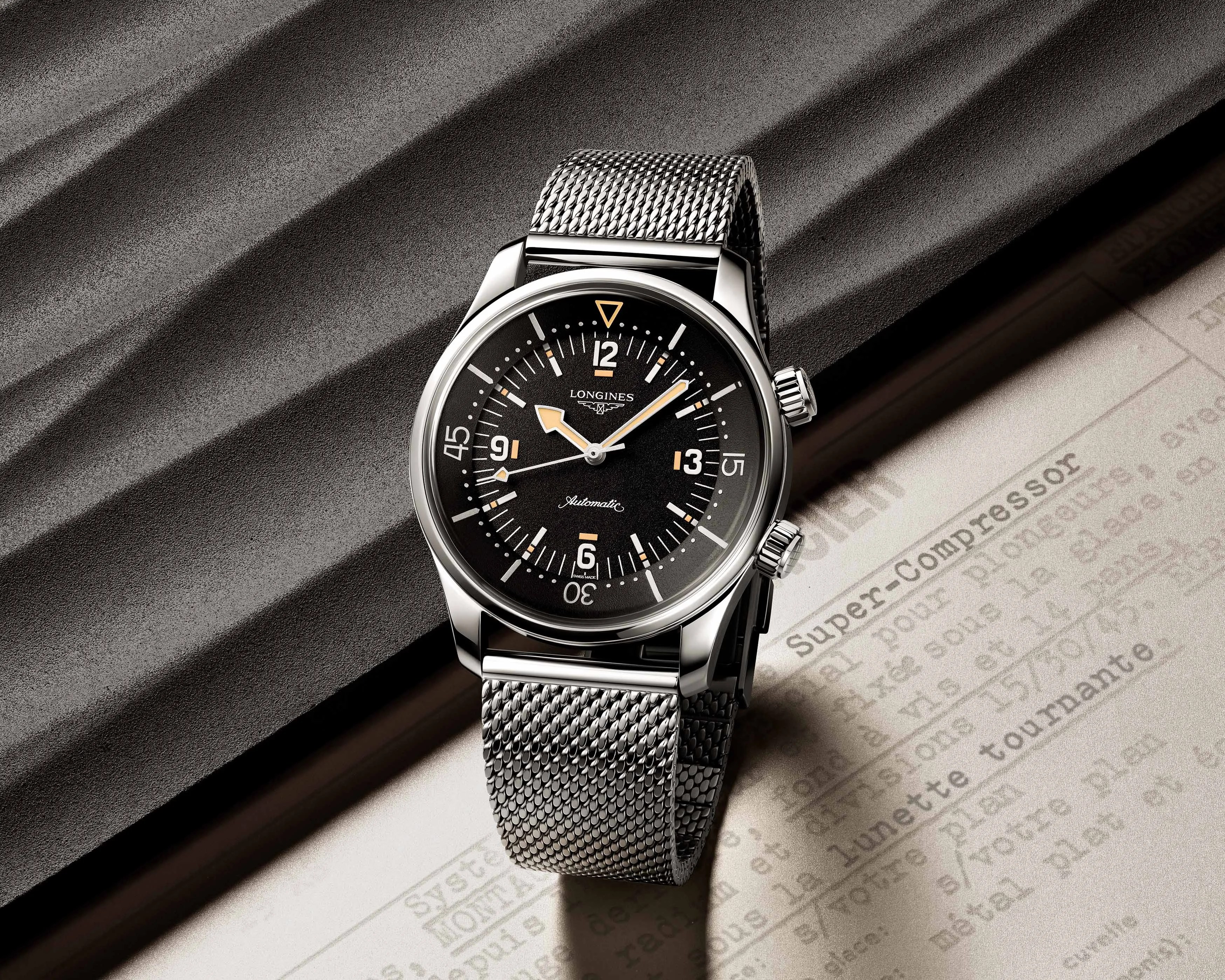 Silver Longines wristwatch with black dial and mesh metal strap on textured surface.