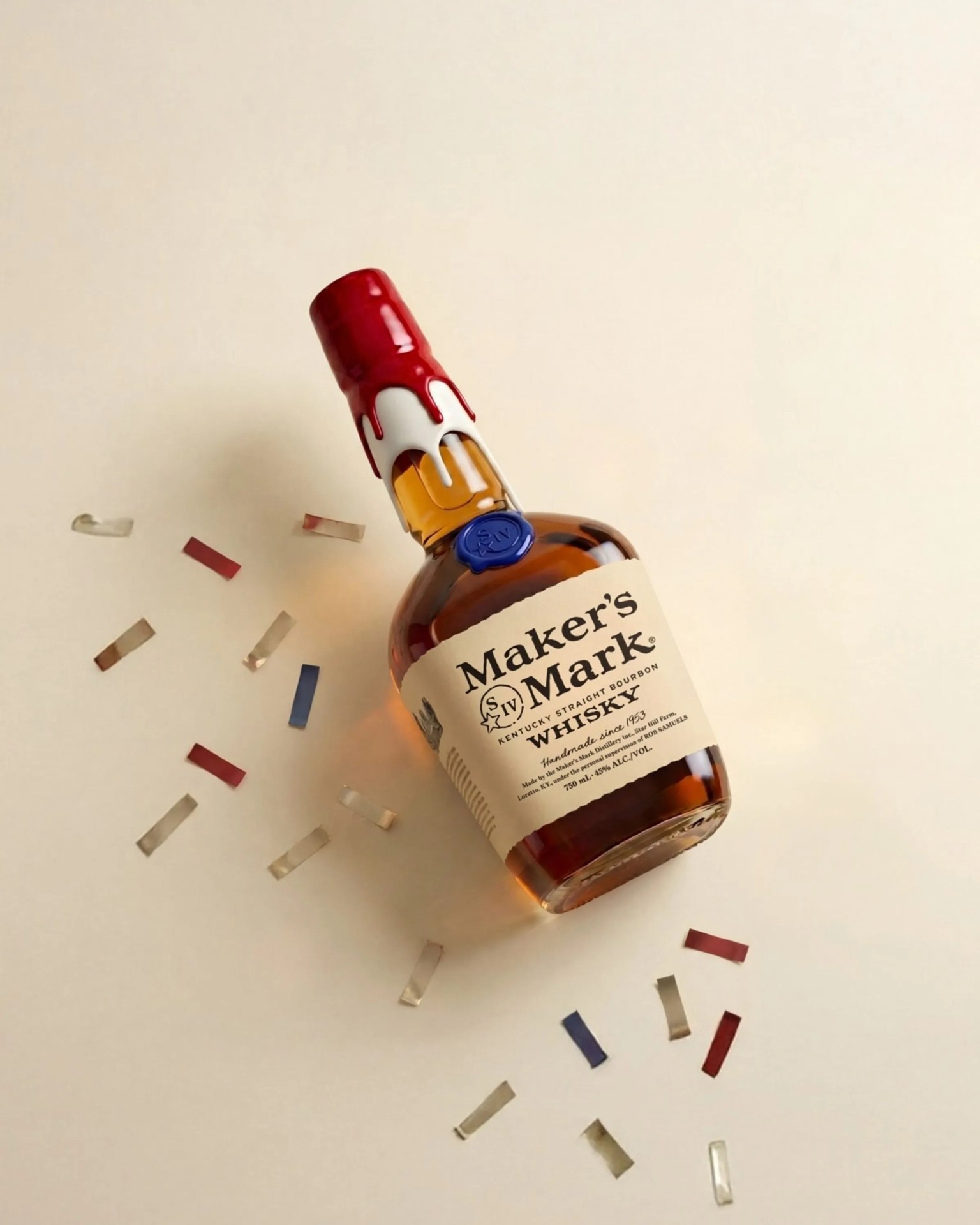 Bottle of Maker's Mark Kentucky Straight Bourbon Whisky with red wax seal and scattered confetti on a beige surface.
