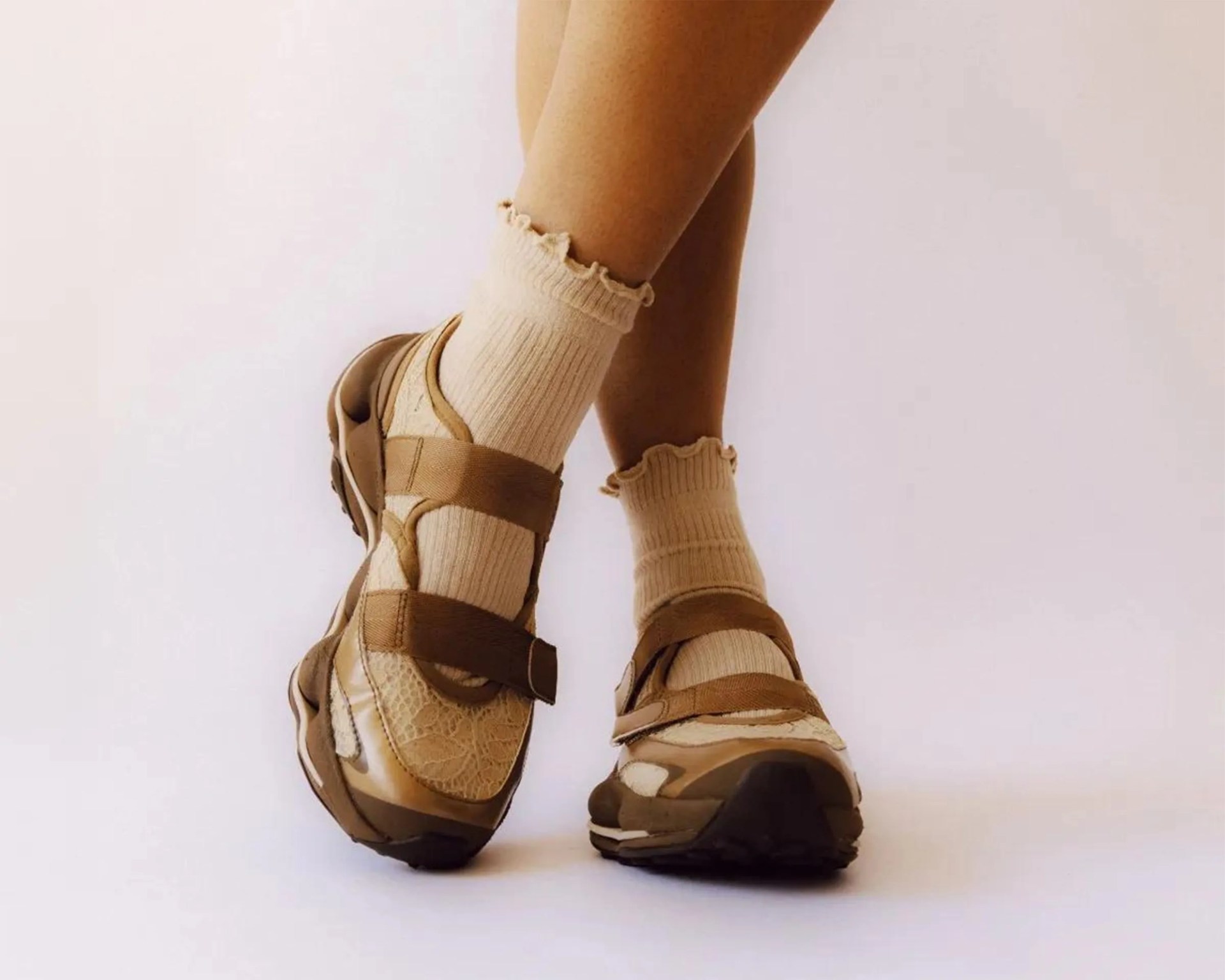 Beige textured sneakers with brown straps worn with cream ruffled ankle socks.