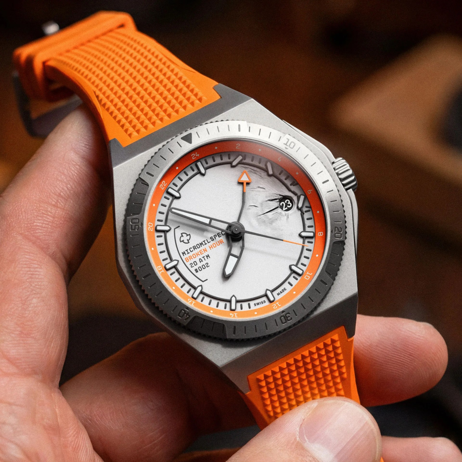 Close-up of a wristwatch with a silver case, orange textured rubber strap, and a white dial featuring orange and black accents.