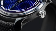 Close-up of a watch with a textured deep blue dial, silver case, and a black woven strap.