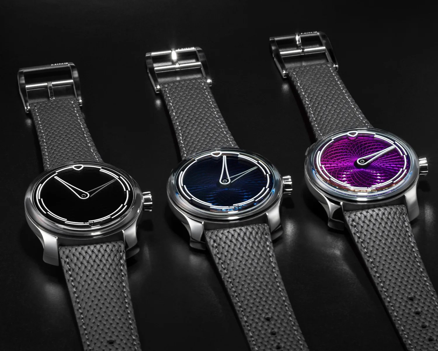 Three wristwatches with textured gray straps and polished silver cases, featuring black, blue, and purple dials with minimalist white markings.