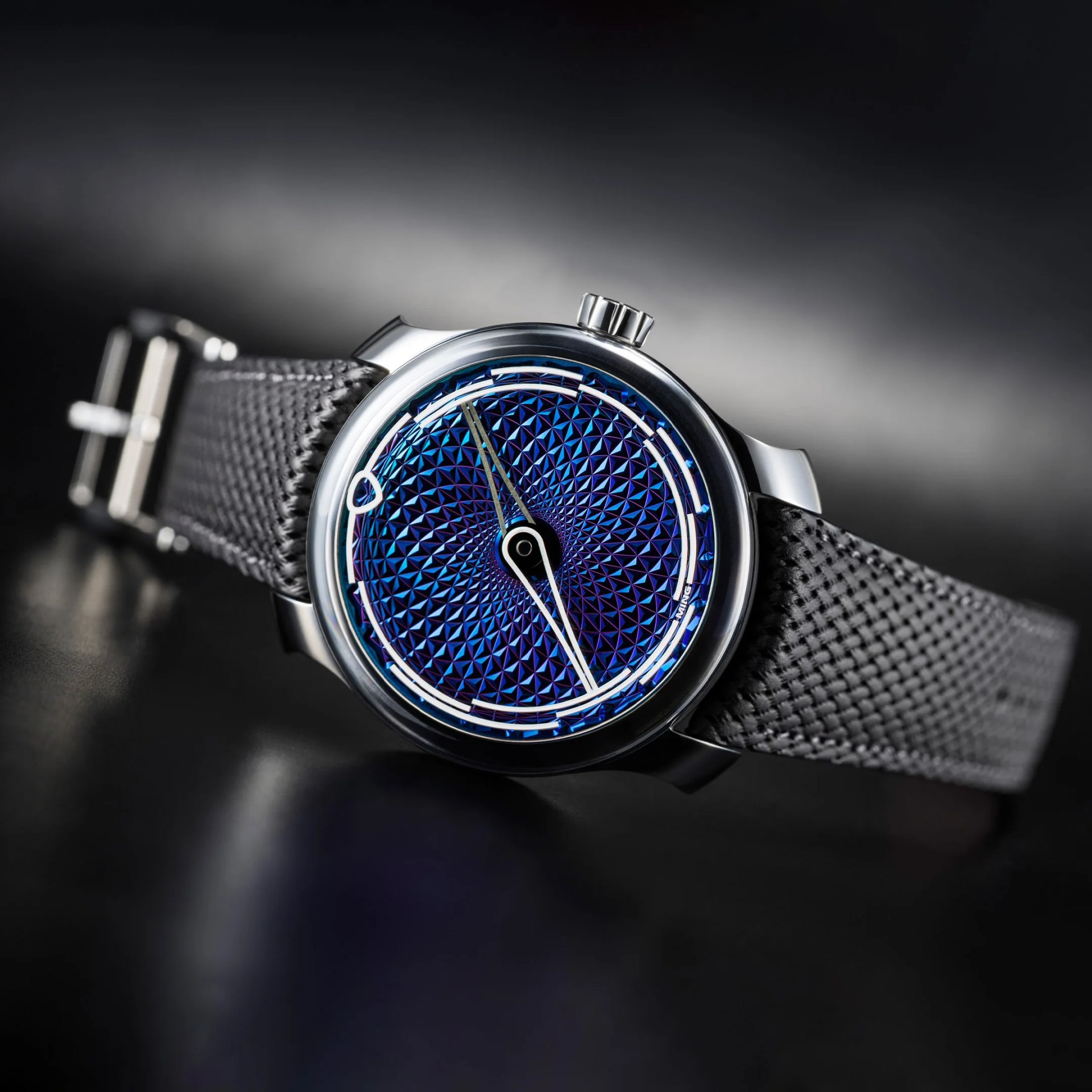 Close-up of a wristwatch with a textured blue dial, silver case, and black woven strap.