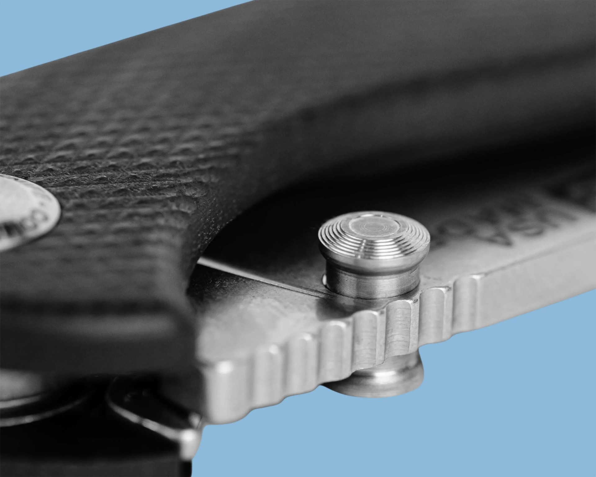 Close-up of a textured black handle and a silver metal screw on a mechanical device against a blue background.