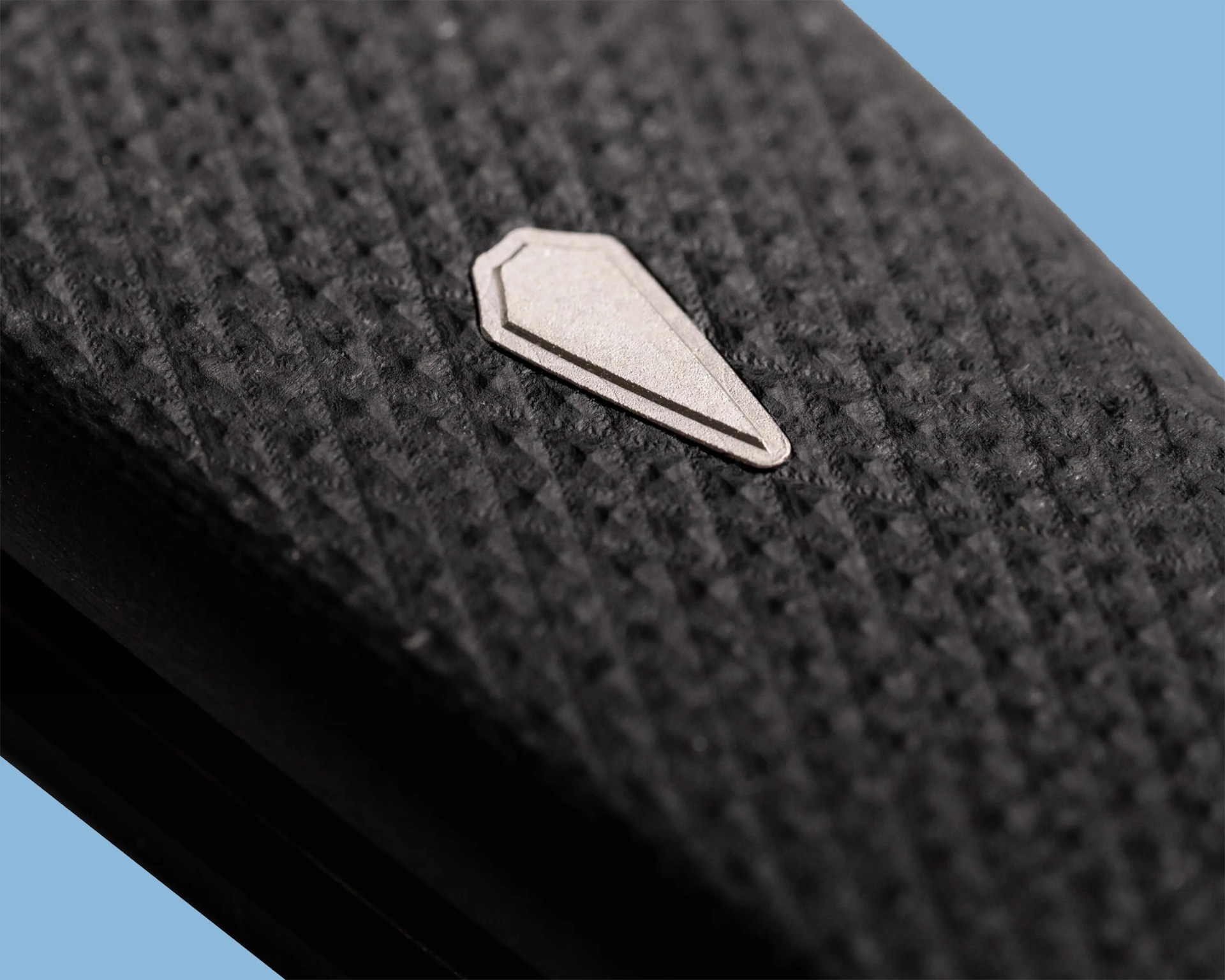 Close-up of a textured black surface with a small, light gray, coffin-shaped emblem in the center.