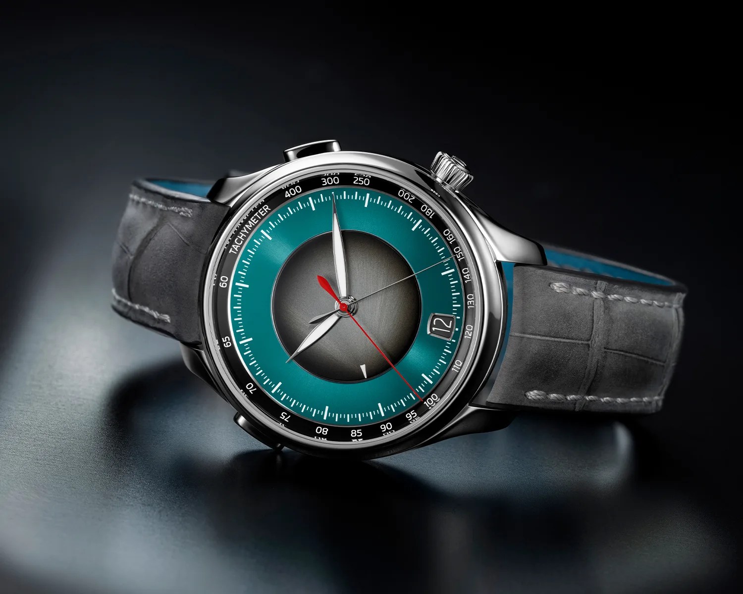 Silver wristwatch with teal and gray dial, red second hand, date window, and gray leather strap on a dark surface.