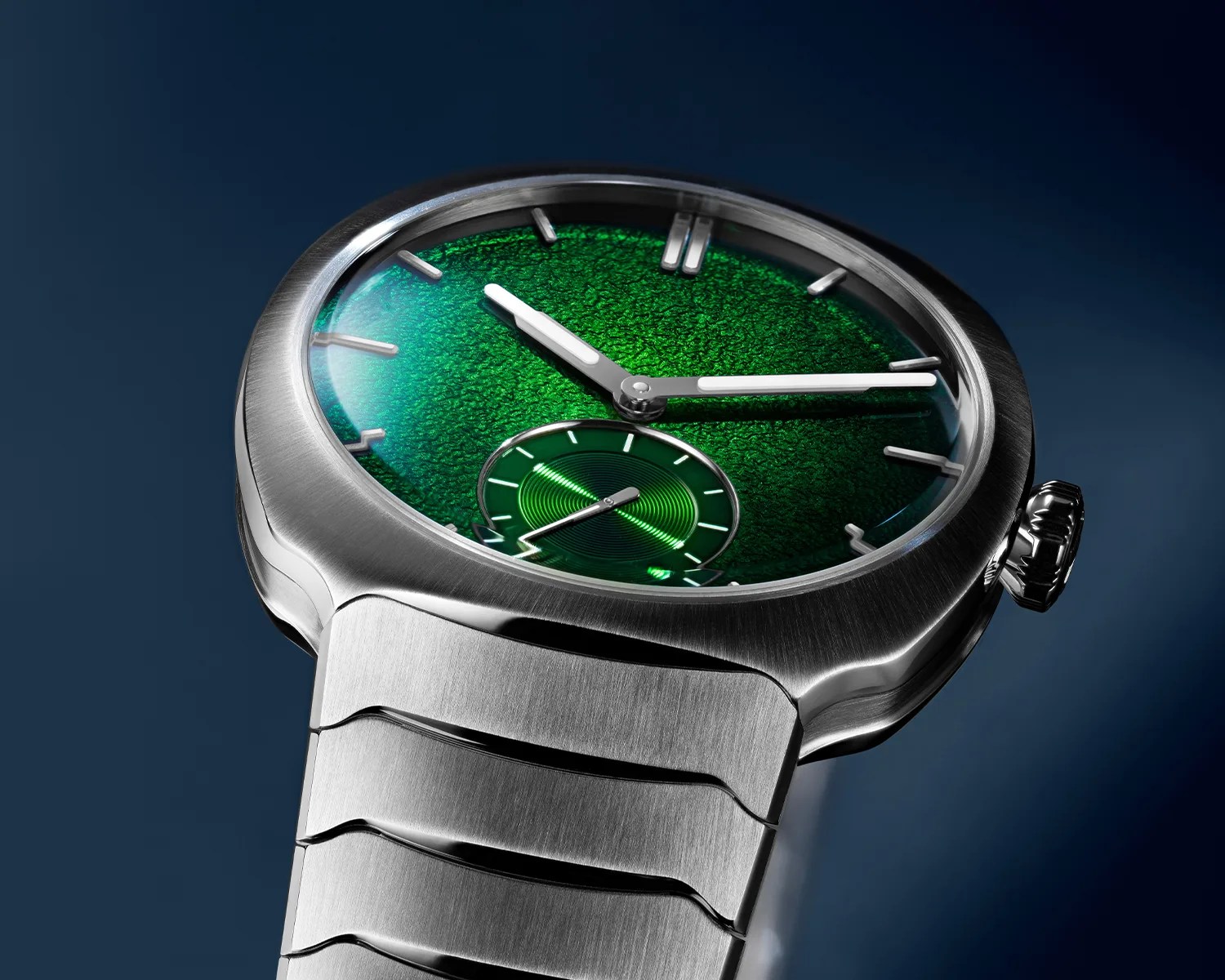 Silver metal wristwatch with a textured green dial and a small seconds subdial on a dark background.