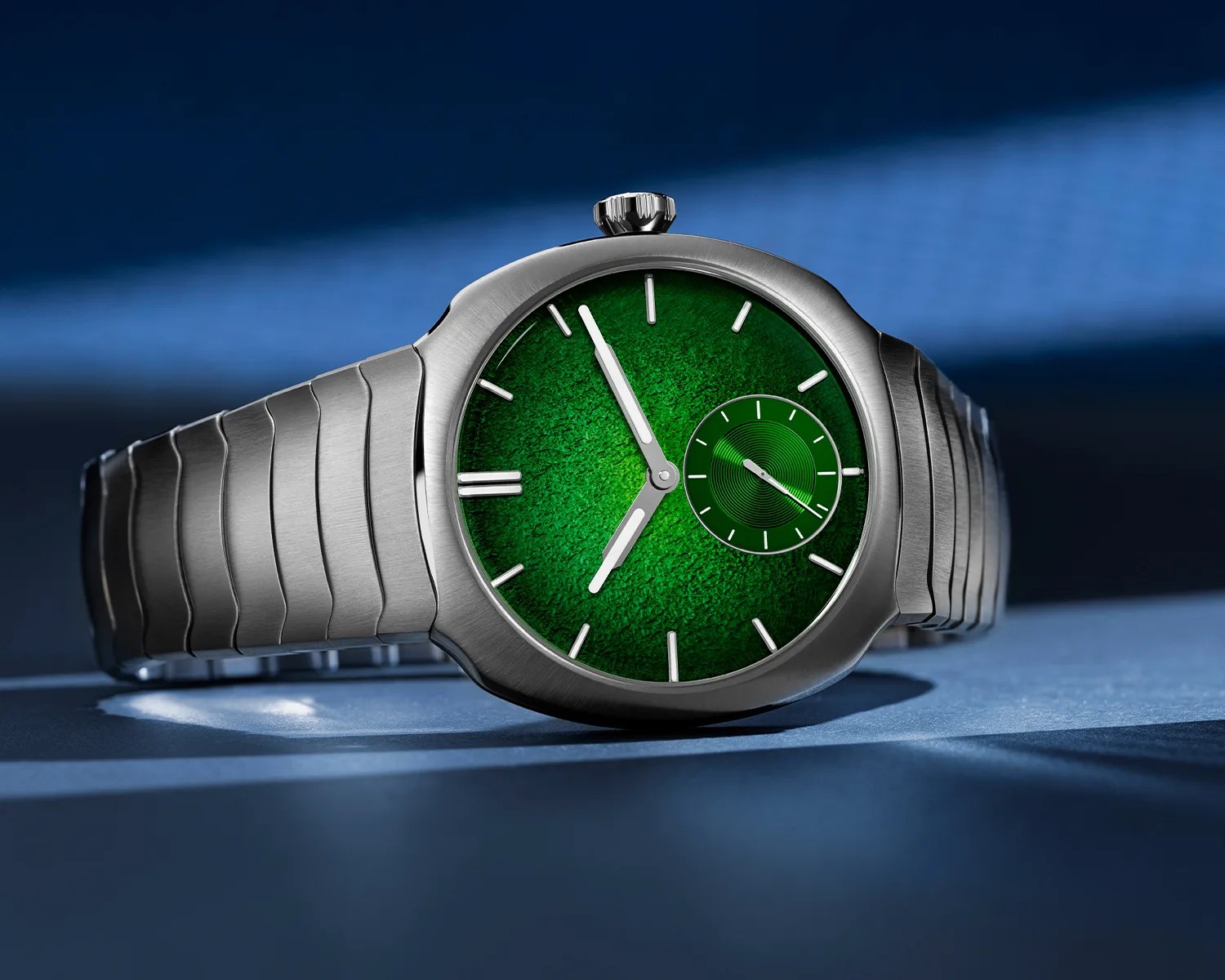 Silver metal wristwatch with a textured green dial and a small subdial on a blue surface.