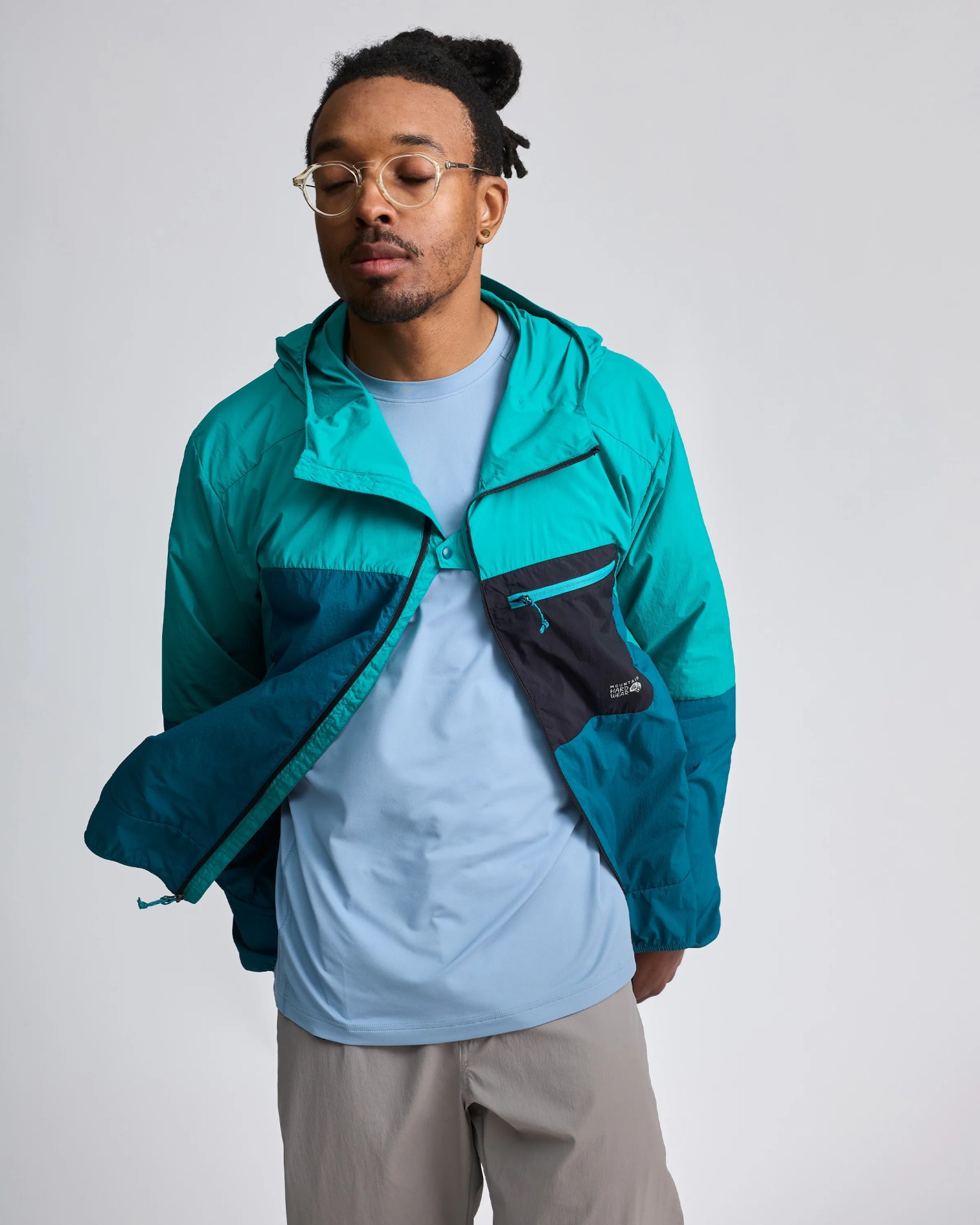 Teal and navy color-block windbreaker jacket with a zippered chest pocket worn over a light blue shirt.