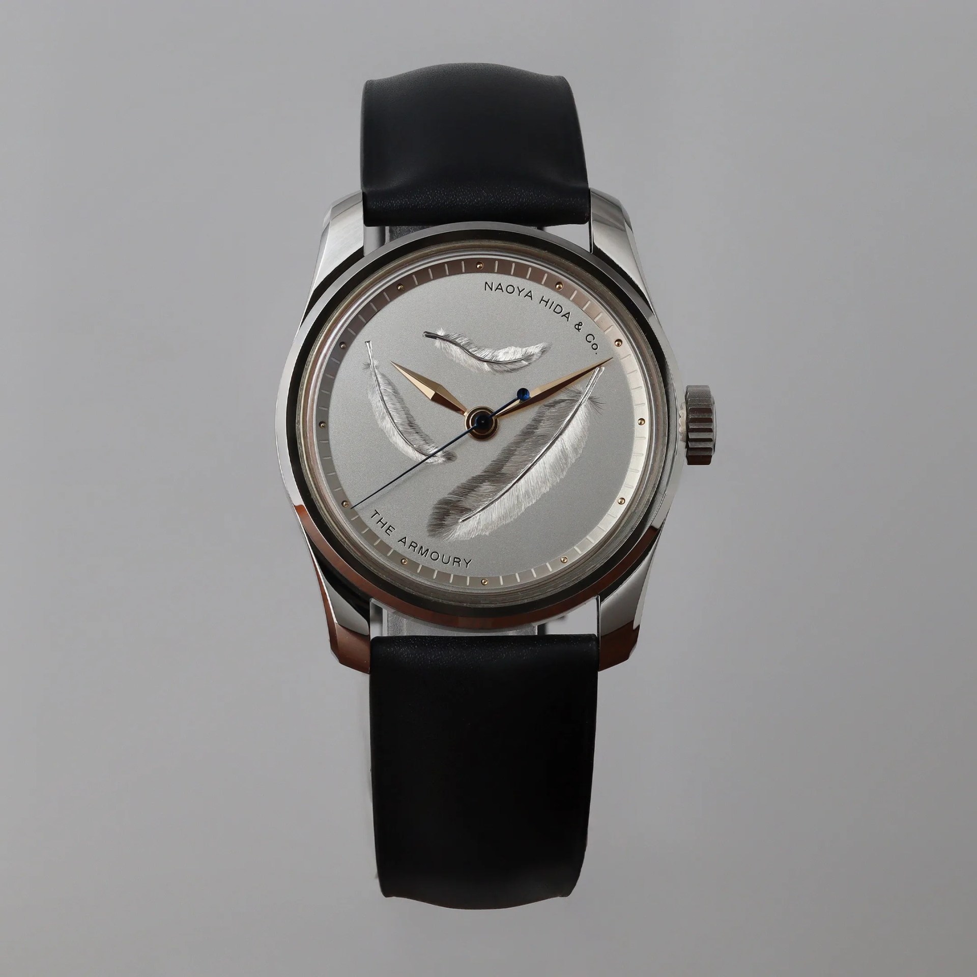Silver wristwatch with black leather strap and feather designs on the dial, labeled "Naoya Hida & Co." and "The Armoury.