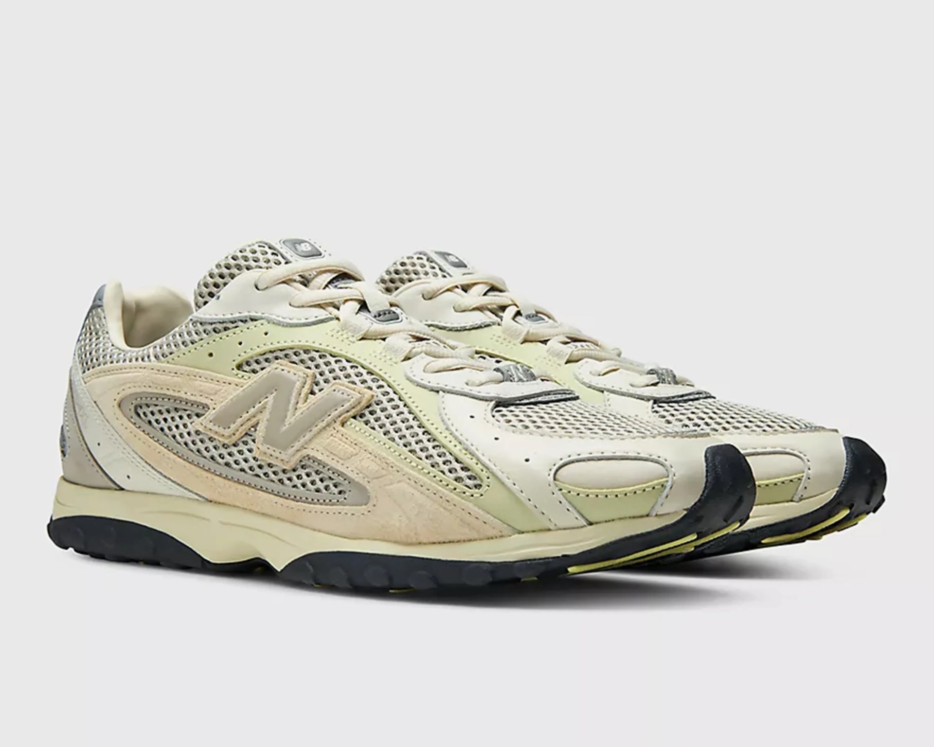 Pair of beige and cream New Balance mesh and suede sneakers with black and yellow soles.