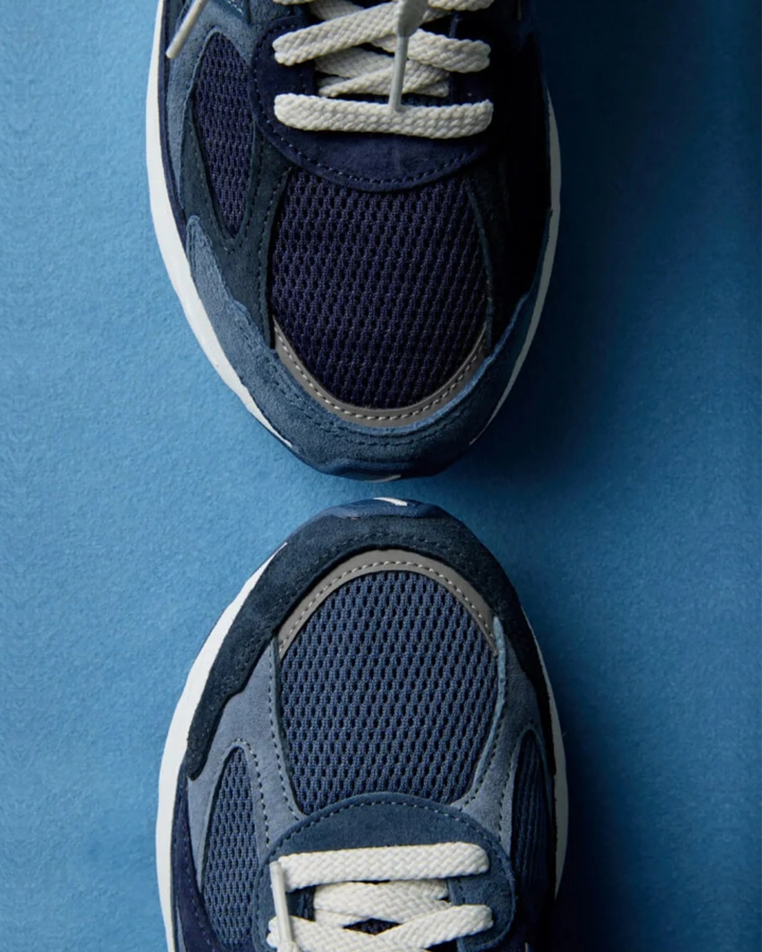 Pair of navy blue sneakers with white laces and mesh fabric on a blue surface.