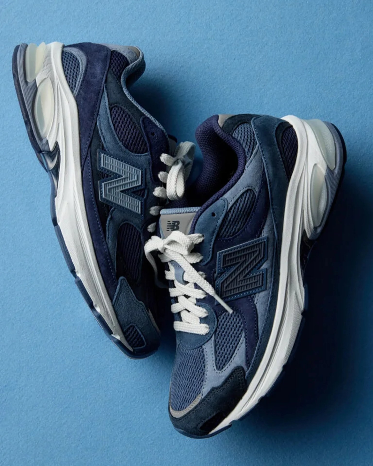 Pair of navy blue New Balance sneakers with white soles and laces on a blue background.