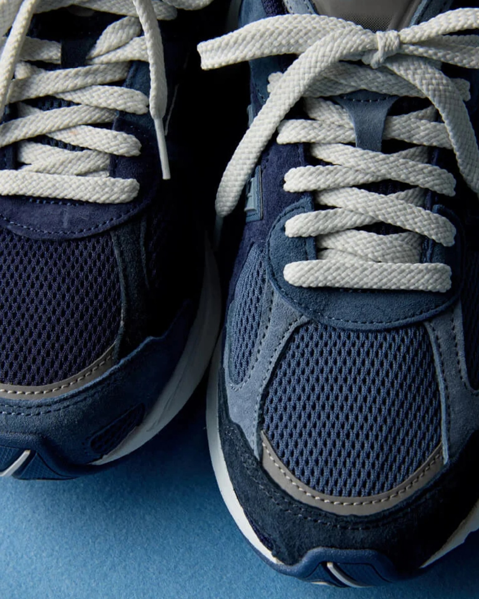 Close-up of navy blue mesh sneakers with thick white laces on a blue surface.