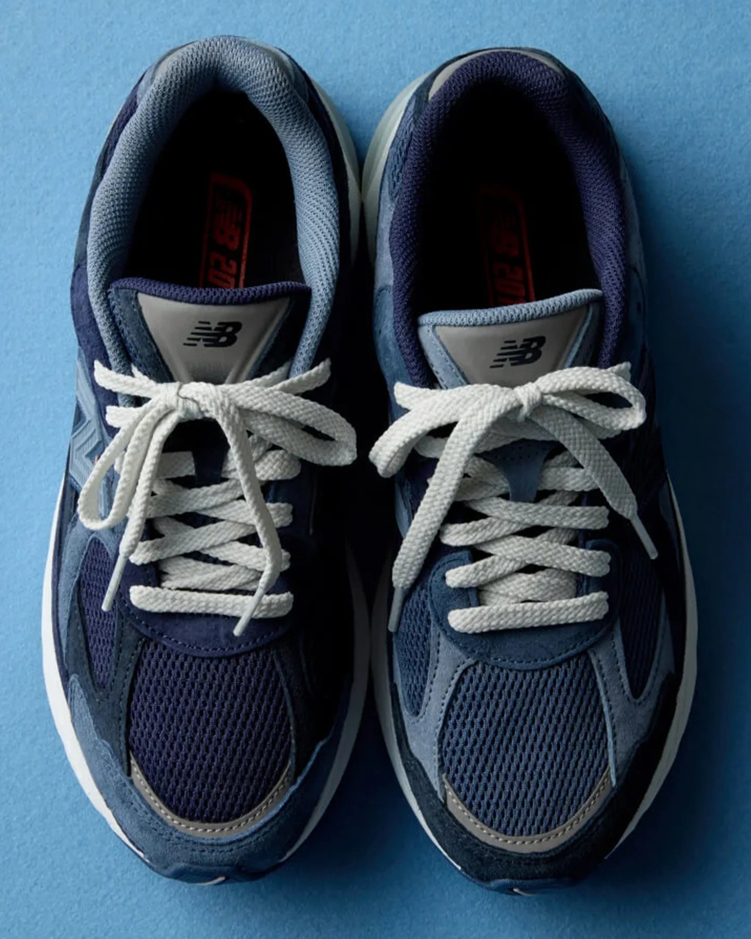 Pair of navy blue New Balance sneakers with white laces on a blue surface.