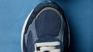 Close-up of a navy blue sneaker toe with mesh and suede panels and white laces on a blue surface.