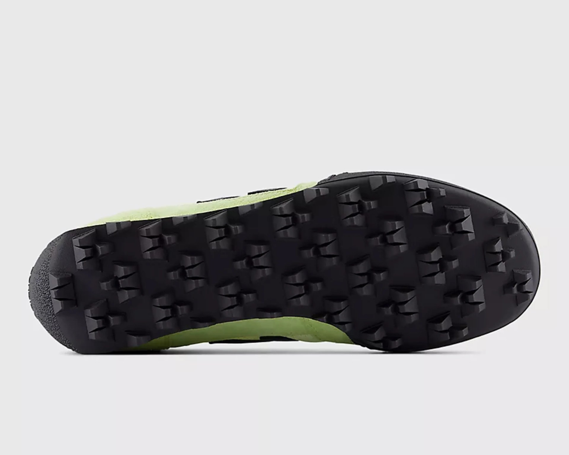 Black rubber outsole with deep, angular treads on a green shoe sole.