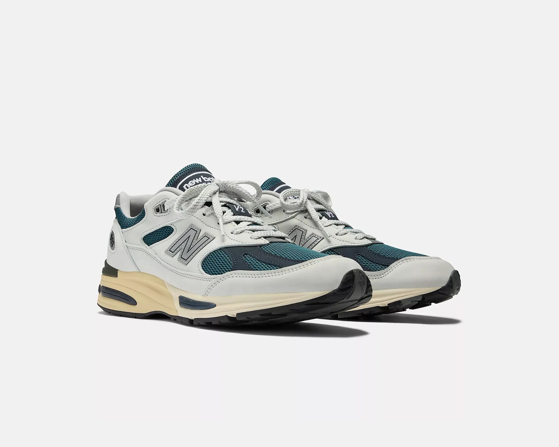 Pair of white and teal New Balance sneakers with beige midsoles and black outsoles on a white background.