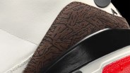 Close-up of a sneaker showing white leather, brown textured suede with black patterns, black smooth leather, and a red textured sole.