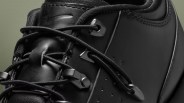 Close-up of black leather sneaker with black laces threaded through metal eyelets and hooks.