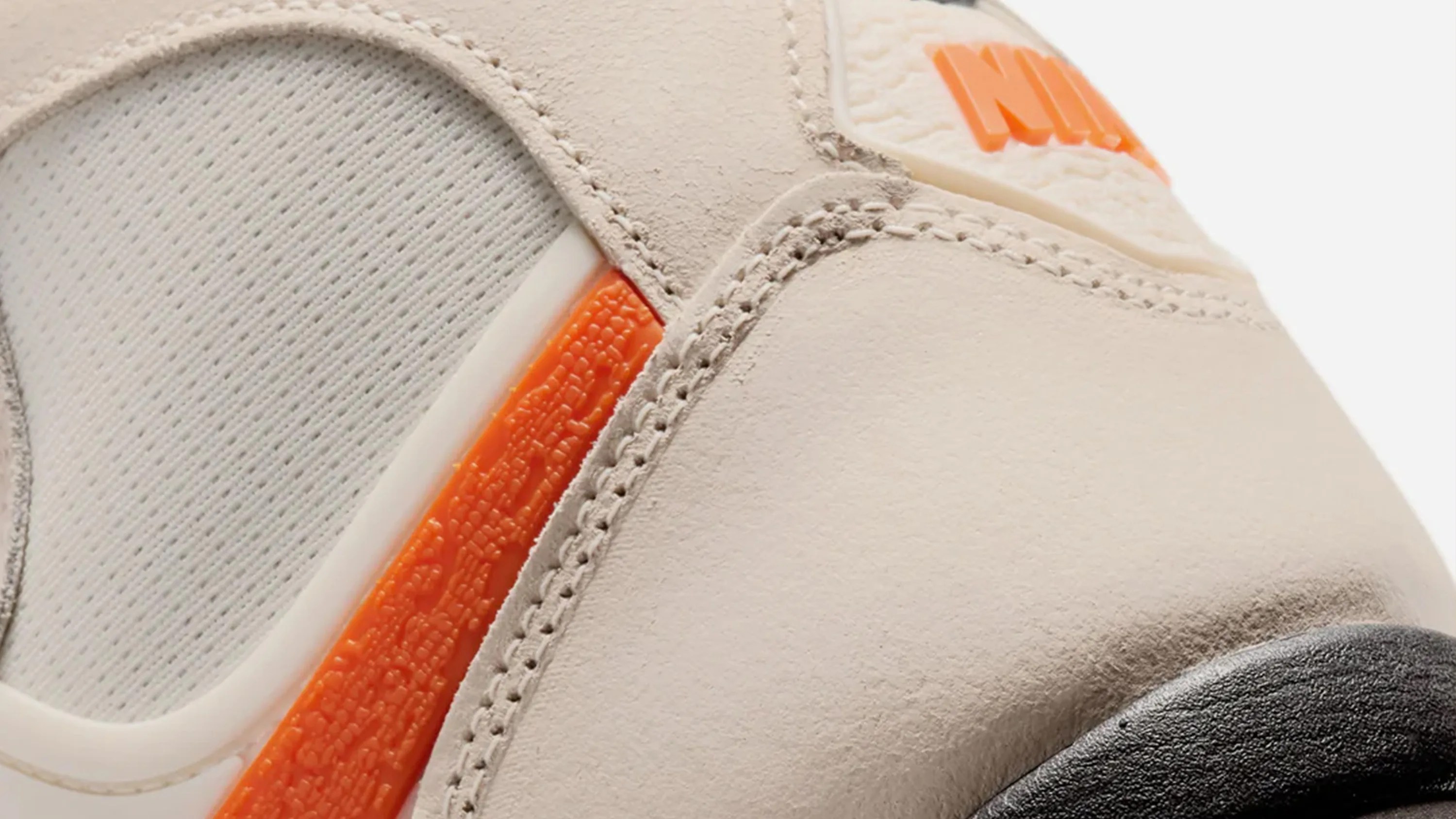 Close-up of beige Nike sneaker with orange textured detail and black sole.