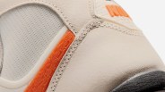 Close-up of beige Nike sneaker with orange textured detail and black sole.