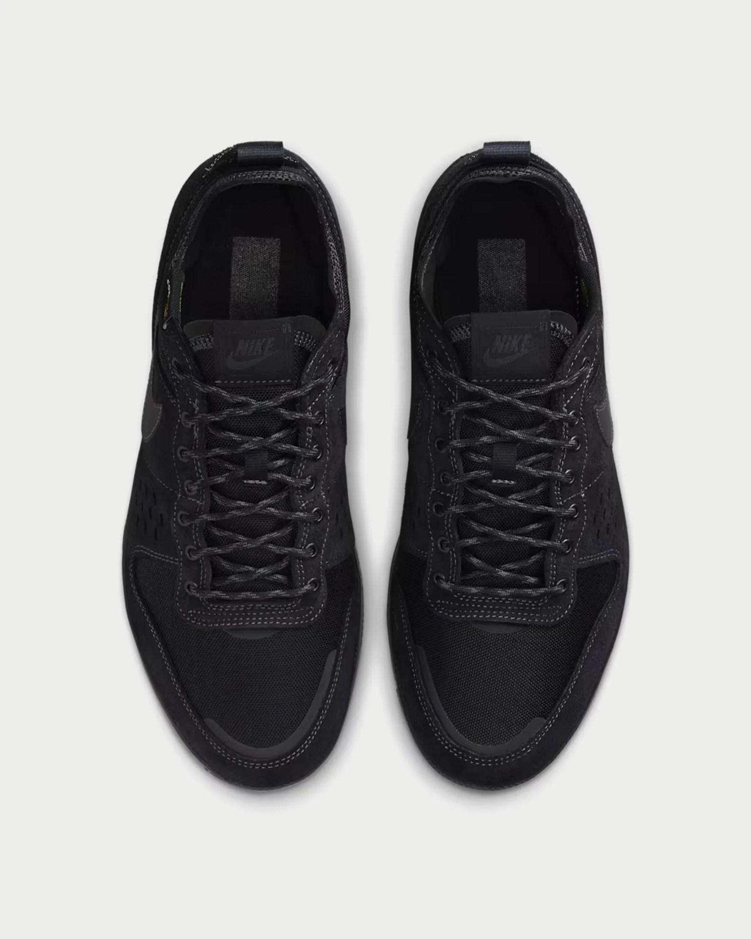 Top view of a pair of black Nike sneakers with black laces on a light gray background.