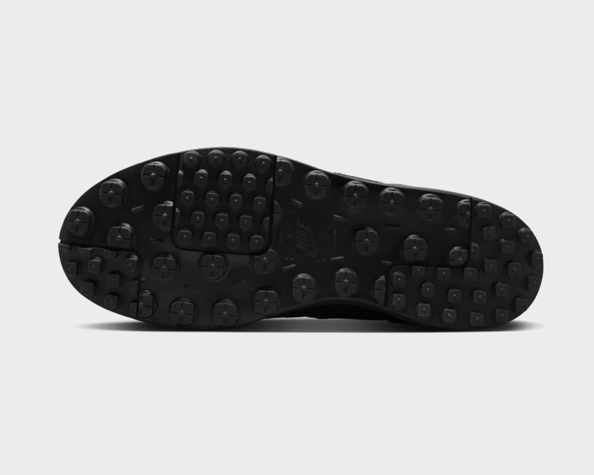 Black rubber shoe sole with square and circular tread patterns and a visible Nike logo.