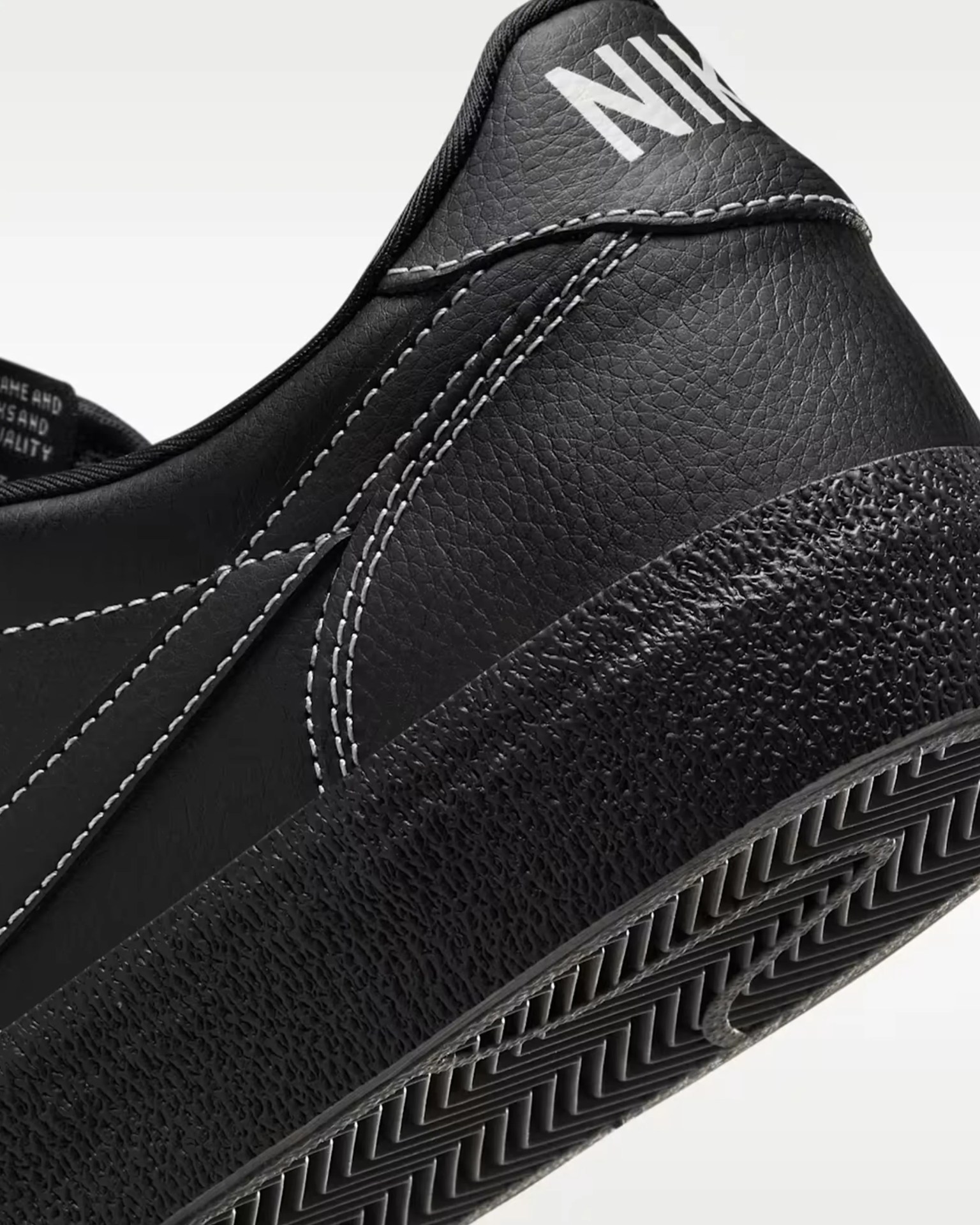 Close-up of black Nike shoe heel with textured sole and white stitching on leather upper.