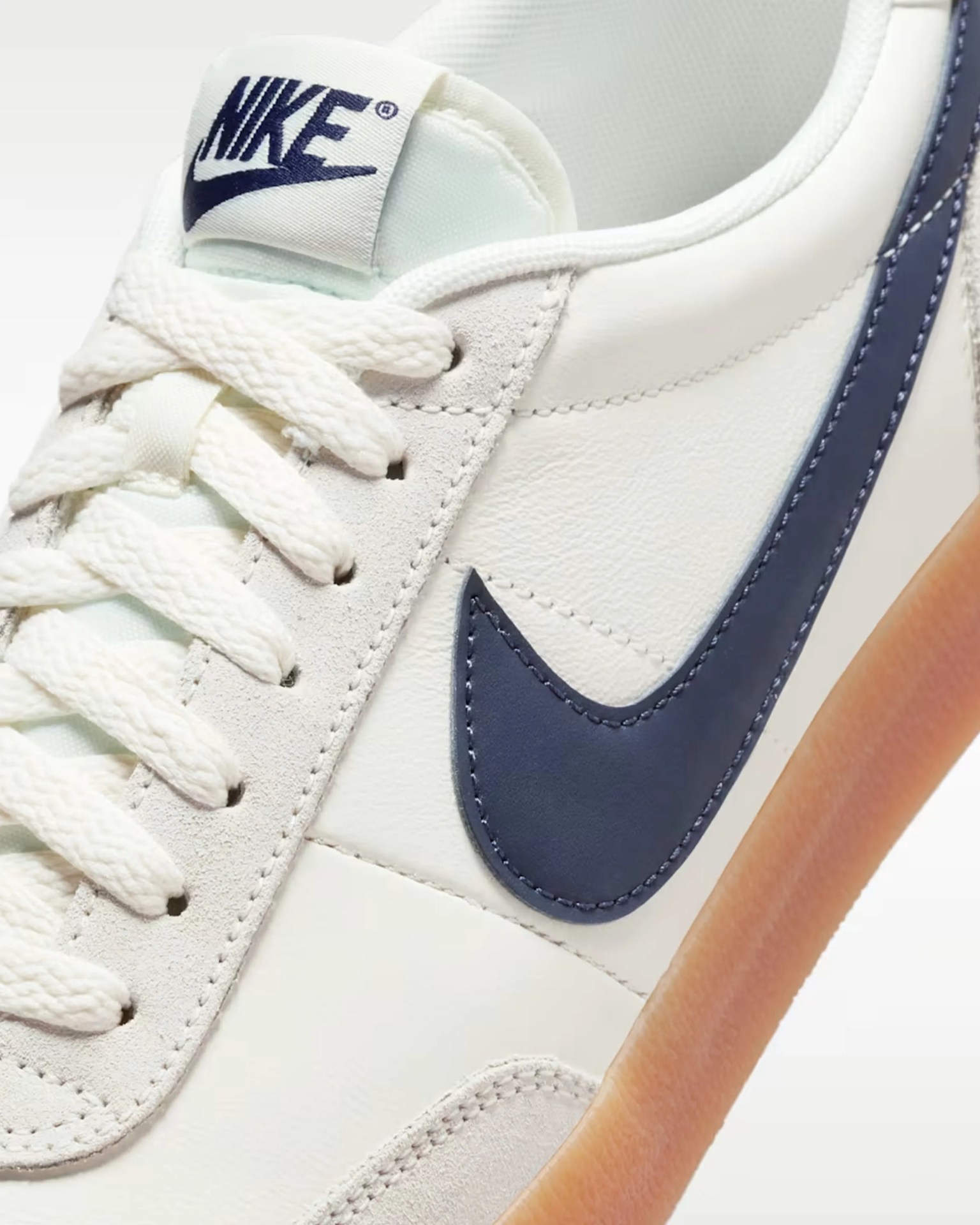 Close-up of white Nike sneaker with navy blue swoosh and gum sole, showing laces and tongue label.
