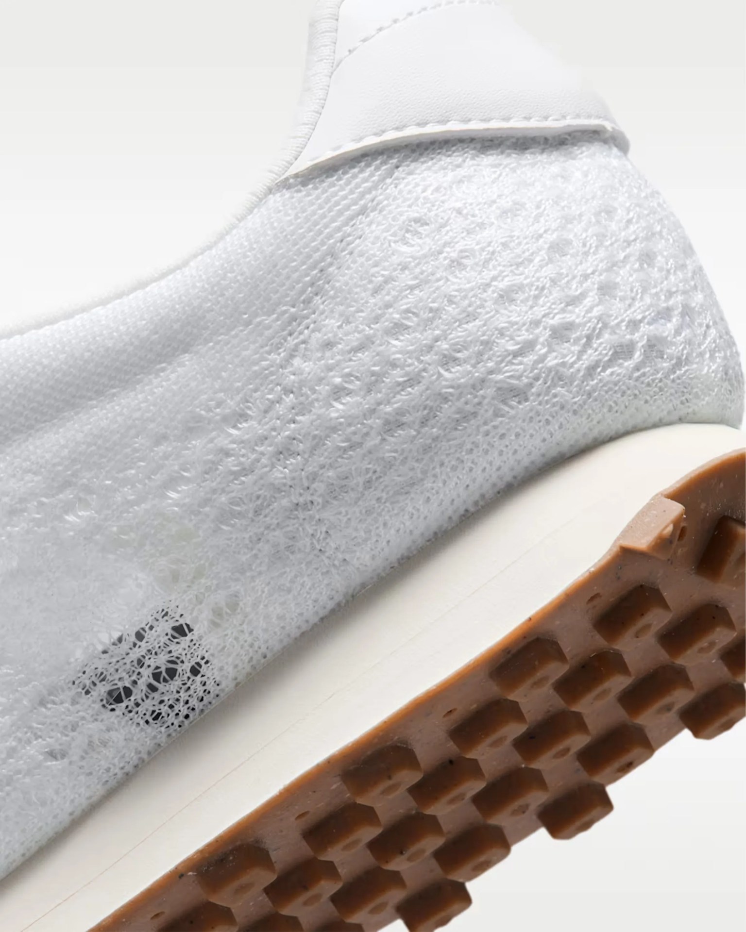 Close-up of a white sneaker heel with textured knit upper and brown rubber outsole with square studs.