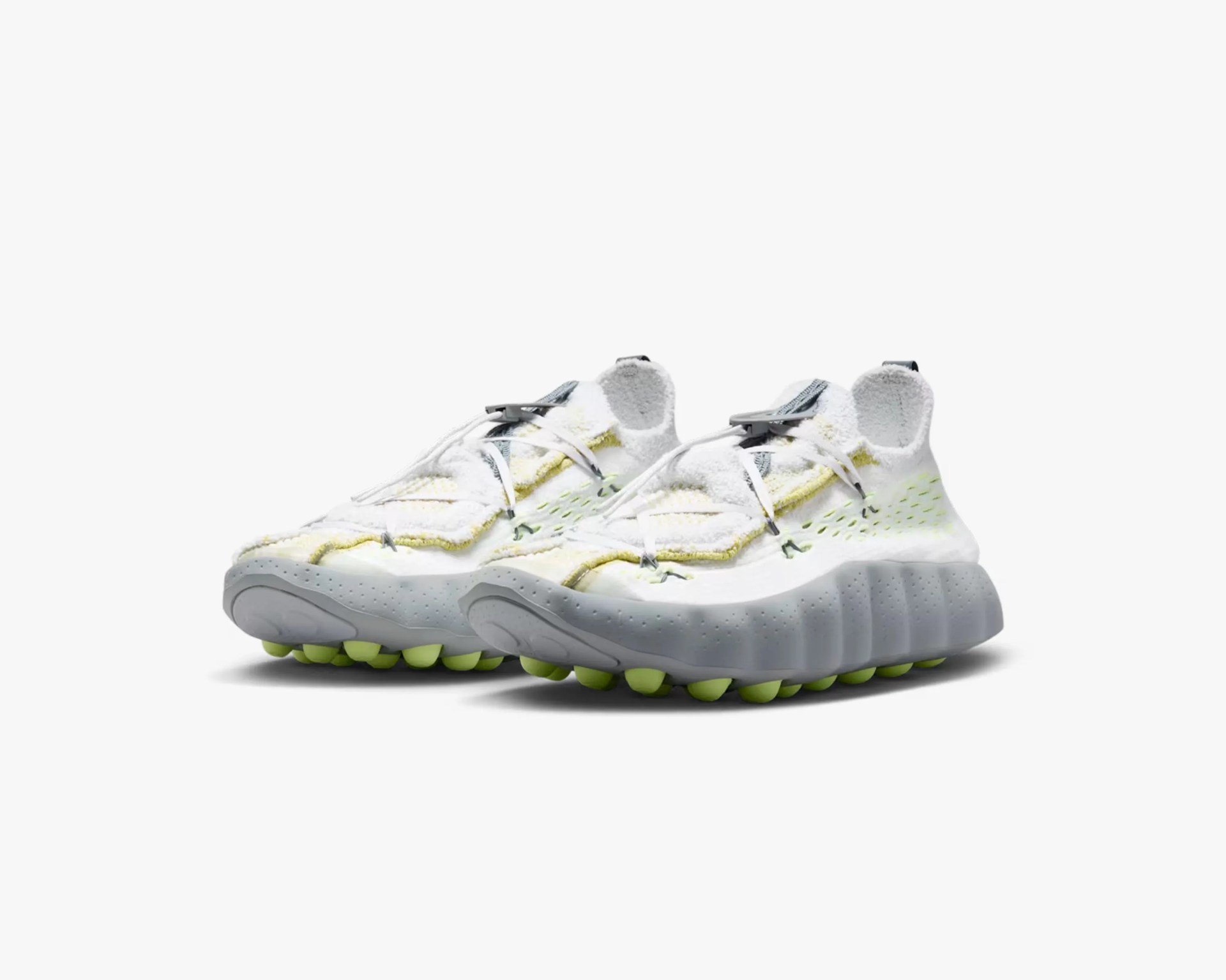 White and light yellow athletic shoes with textured gray soles and neon green tread.