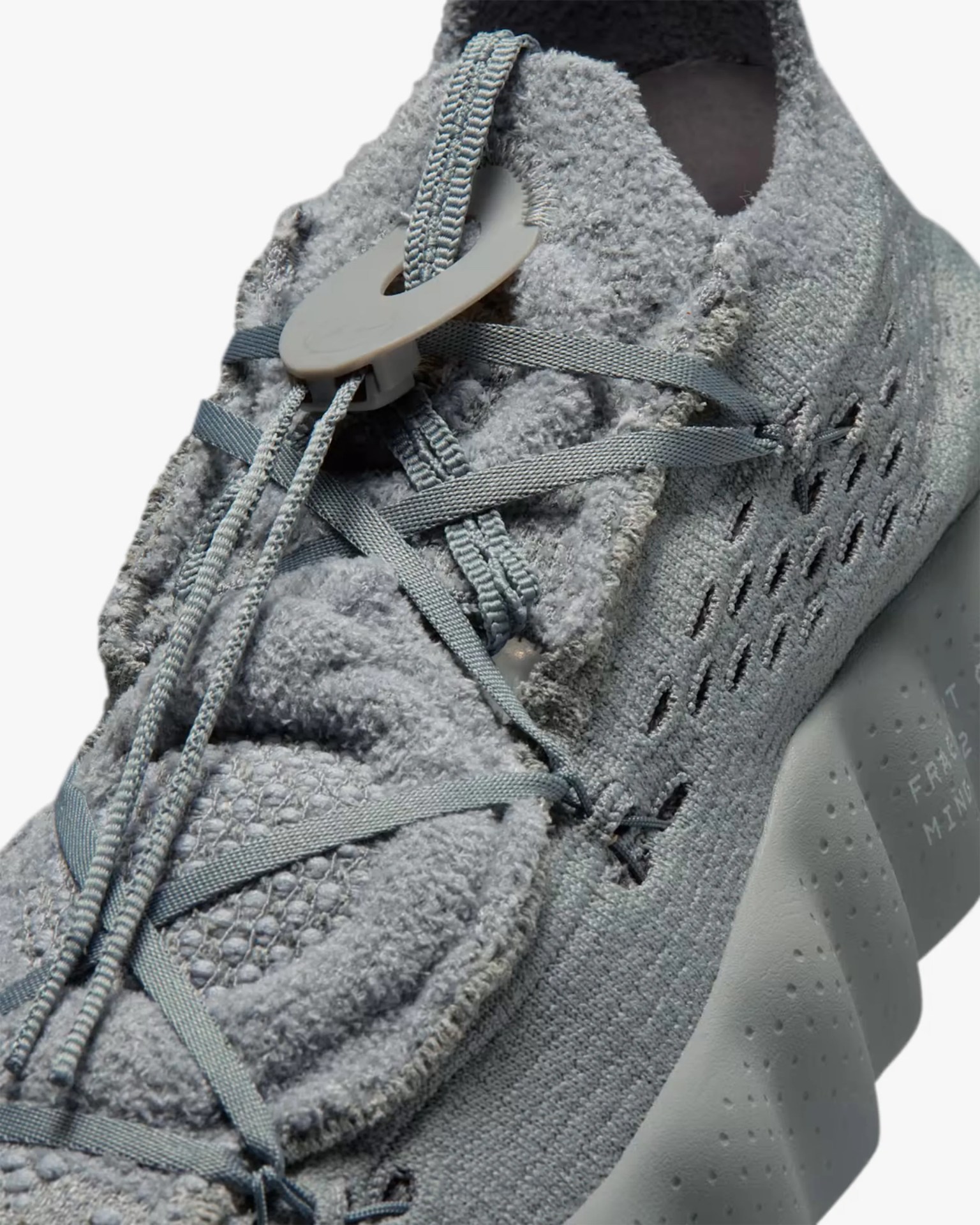Close-up of a light gray textured sneaker with flat and round laces secured by a plastic toggle.