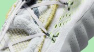 Close-up of a white and yellow textured sneaker with light gray laces and perforated sole against a green background.