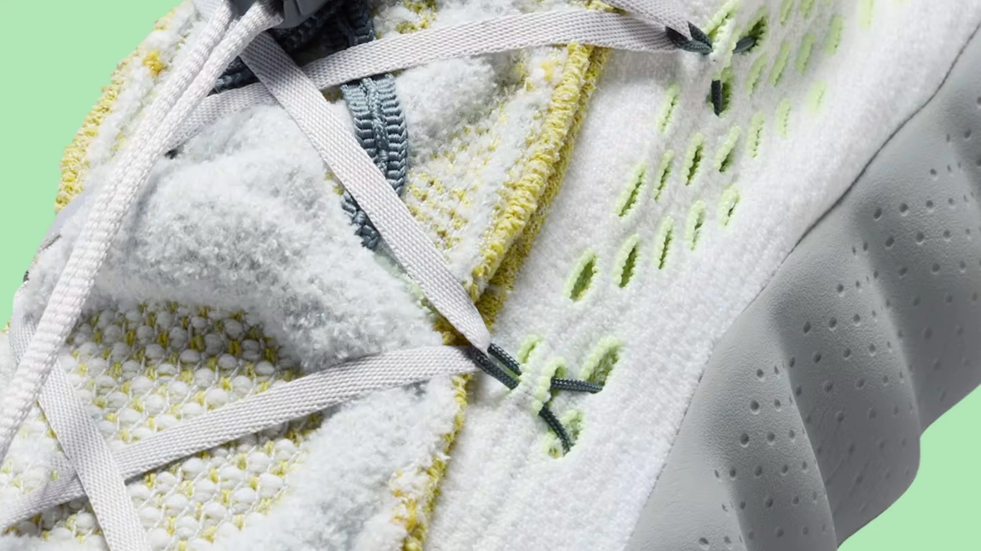 Close-up of a white and yellow textured sneaker with light gray laces and perforated sole against a green background.
