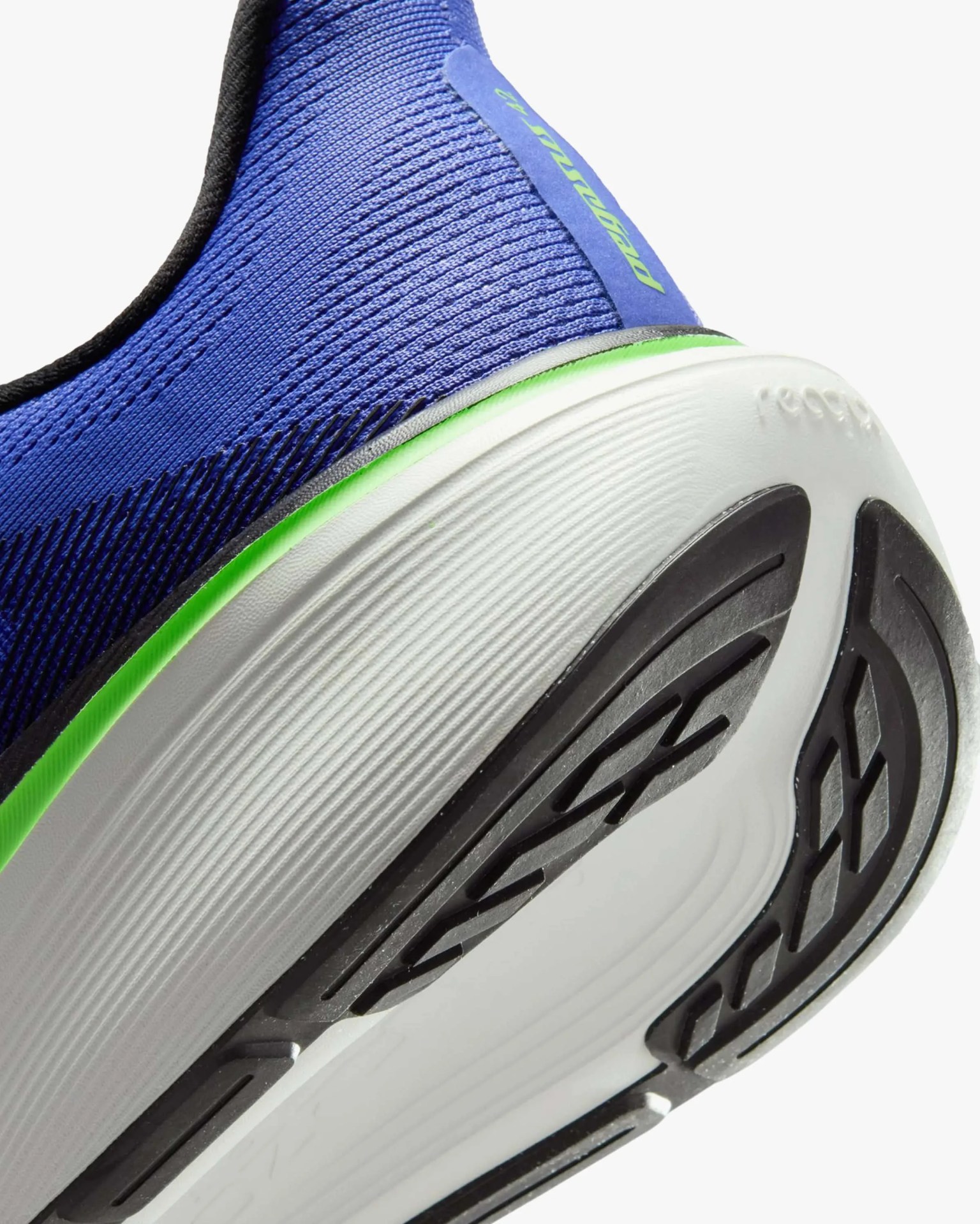 Close-up of the heel and sole of a blue athletic shoe with a white midsole, green accent, and black tread.