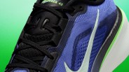 Close-up of a blue and black Nike Pegasus 42 running shoe with black laces and a white swoosh on a green background.