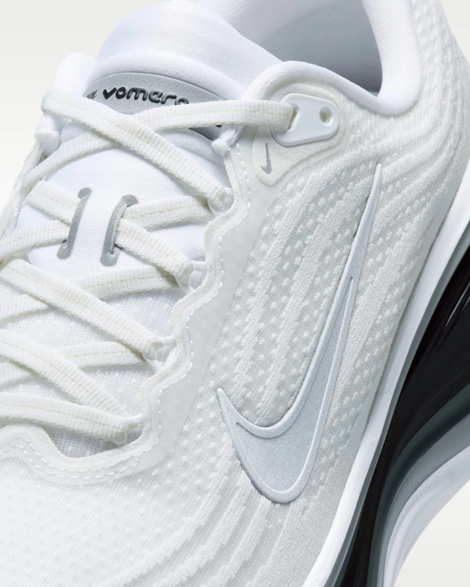 Close-up of white Nike Air Max sneaker with textured fabric, white laces, and silver swoosh logo.