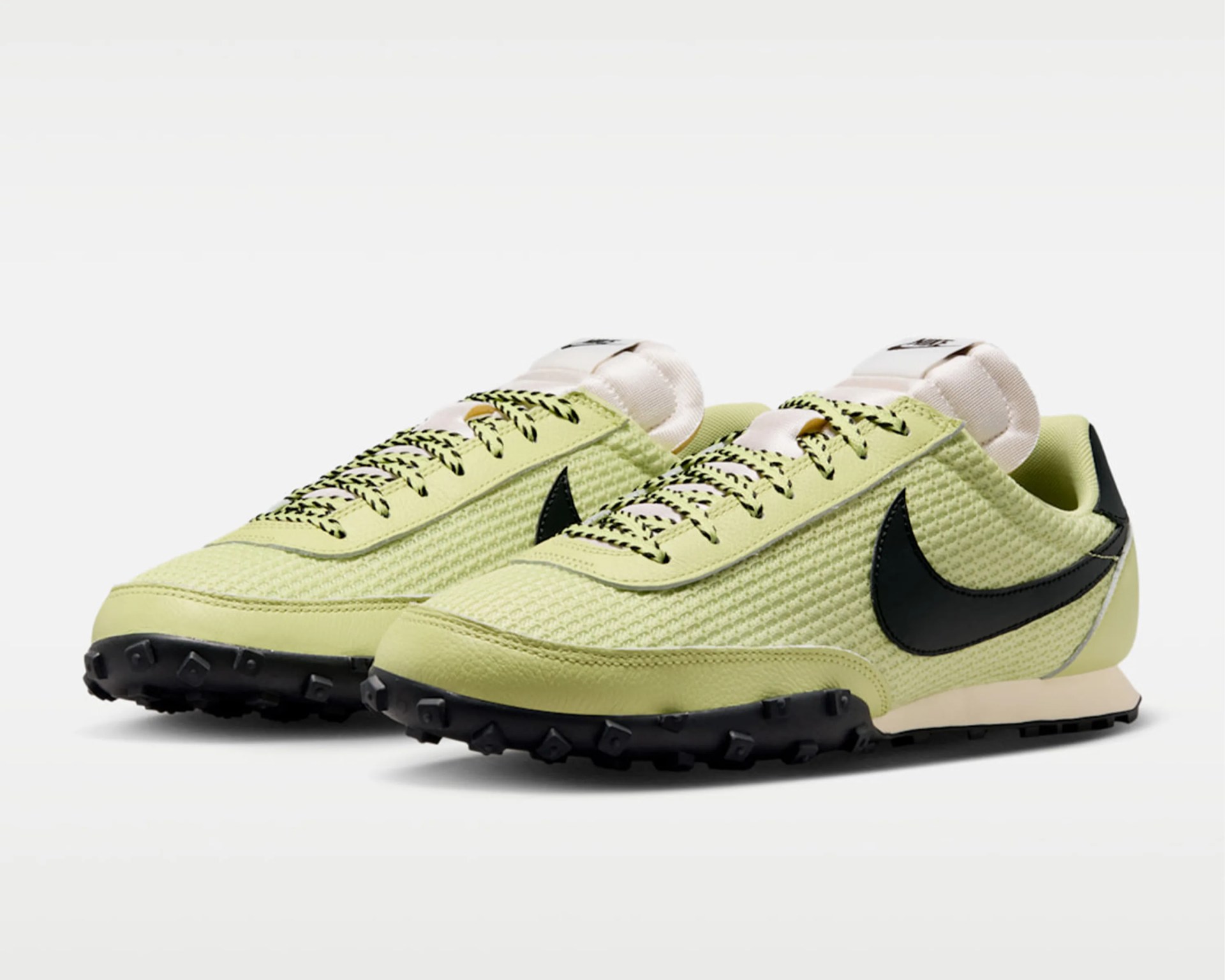 Pair of light green Nike sneakers with black swoosh logos and black patterned laces on a white background.